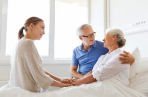 A woman holding the hands of an elderly woman in a hospital bed.
