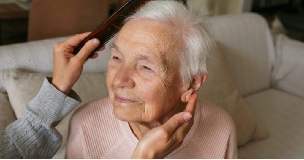 Elderly woman with white hair being gently brushed.